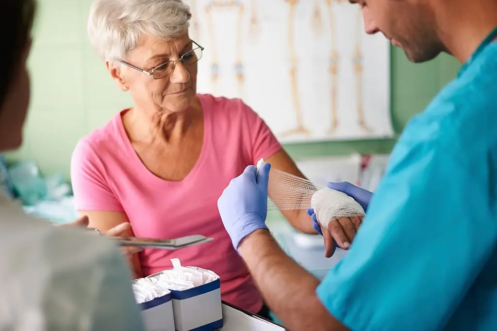 Healthcare Professional Applying Bandage To Senior Woman’s Hand During Advanced Wound Care Edmonton Treatment In A Clinical Setting.