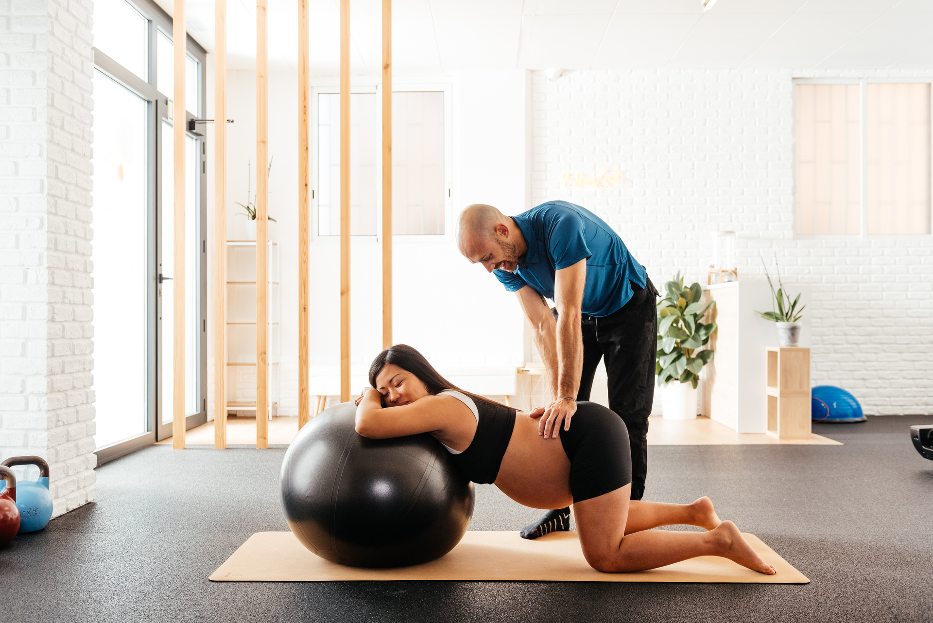 Pregnant Woman Performing Exercise On A Stability Ball With Physiotherapist Support During Prenatal Physio Session In A Bright Clinic. Pregnant Woman Performing Exercise On A Stability Ball With Physiotherapist Support During Prenatal Physio Session In A Bright Clinic.
