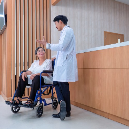 A Patient Sitting In A Wheelchair In A Hospital Hallway Near An Information Desk, Representing Accessible Care And Mobility Support During Physiotherapy Edmonton At In Step Physical Therapy. A Patient Sitting In A Wheelchair In A Hospital Hallway Near An Information Desk, Representing Accessible Care And Mobility Support During Physiotherapy Edmonton At In Step Physical Therapy.
