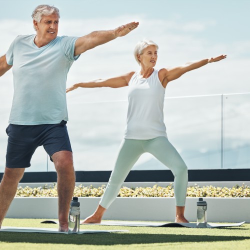 An Active Senior Couple Practicing The Yoga Warrior Pose And Meditation During A Physiotherapy Edmonton Wellness Session At In Step Physical Therapy. An Active Senior Couple Practicing The Yoga Warrior Pose And Meditation During A Physiotherapy Edmonton Wellness Session At In Step Physical Therapy.