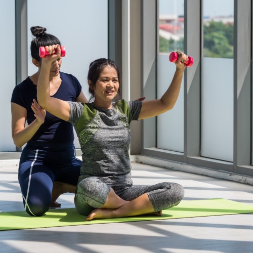 Two Asian Women Practicing Yoga Together In A Gym Setting, Demonstrating The Importance Of Flexibility And Group Wellness During Physiotherapy Edmonton At In Step Physical Therapy. Two Asian Women Practicing Yoga Together In A Gym Setting, Demonstrating The Importance Of Flexibility And Group Wellness During Physiotherapy Edmonton At In Step Physical Therapy.