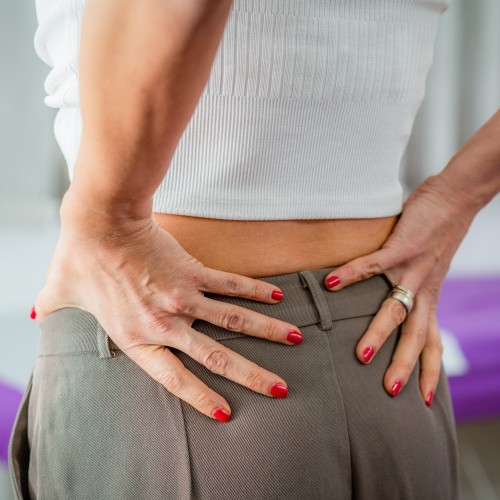 A Woman Massaging Her Lower Back To Alleviate Discomfort, Highlighting The Need For Spinal Care And Rehabilitation During Physiotherapy Edmonton At In Step Physical Therapy. A Woman Massaging Her Lower Back To Alleviate Discomfort, Highlighting The Need For Spinal Care And Rehabilitation During Physiotherapy Edmonton At In Step Physical Therapy.